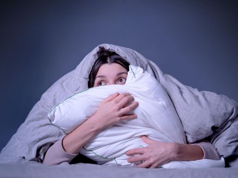 Young girl hugs a pillow and hid under a blanket from all problems, procrastinating, millennials generation. Woman covered with a blanket and is worried about insomnia, poor sleep, getting stress.