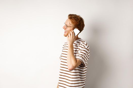 Profile of happy young handsome man talking on mobile phone, looking left and smiling, standing over white background.