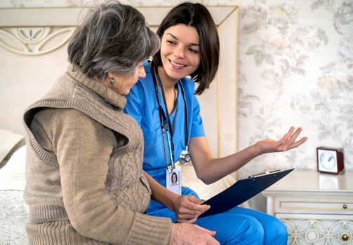 Young nurse is caring for an elderly 80 year-old woman at home, helping her and giving her treatment recommendations. Happy retired woman and trust between doctor and patient. Medicine and healthcare.