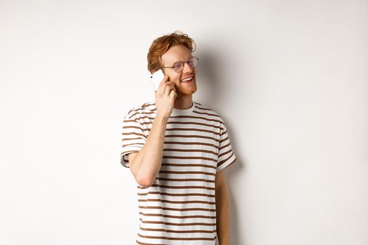 Profile of happy young handsome man talking on mobile phone, looking left and smiling, standing over white background.