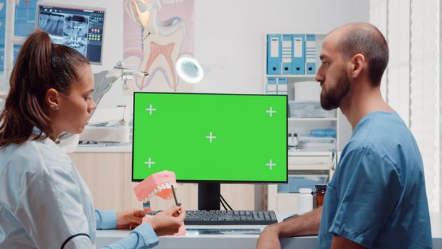 Oral care team looking at horizontal green screen on monitor while analyzing layout of teeth for dental examination. Assistant and dentist using tools and chroma key with mockup template