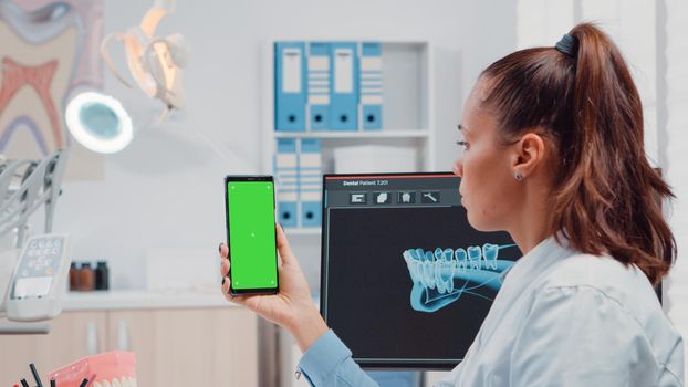 Close up of orthodontist holding smartphone with green screen for oral care and dentistry. Dentist looking at mobile phone with isolated background and mockup template for teethcare
