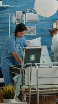 Worried man asking medical team to help sick old wife in nursing home. Doctor and nurse rushing to give assistance to ill retired patient hyperventilating, laying on hospital bed