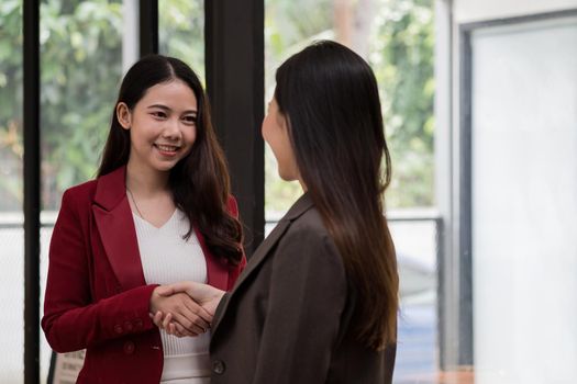 Smiling young businesswoman shaking hands with a coworker during a meeting with colleagues around a table in an office
