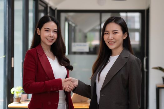 Two confident business asian woman shaking hands during looking at camera in the office, success, dealing, greeting and partner concept.
