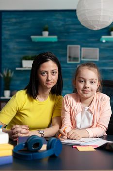 Portrait of smiling family looking into camera while sitting at desk working at mathematics homework during distance school education. Schoolchild studying elementary literature having online lesson