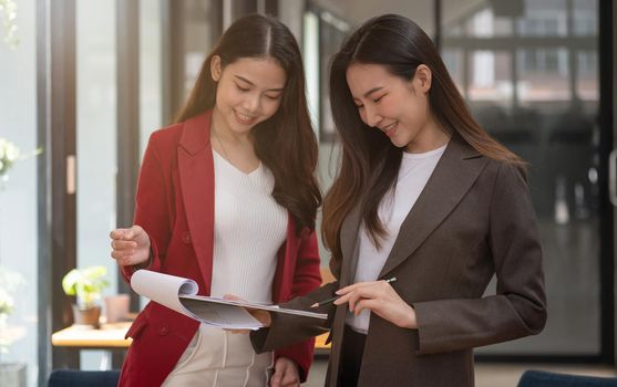Two asian female collegues standing next to each other in an office, business meeting discussion concept.