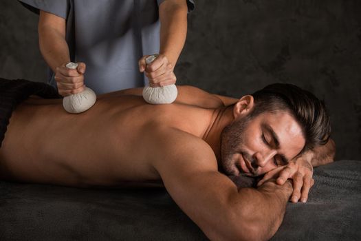 A good-looking man getting a back herbal massage lying down
