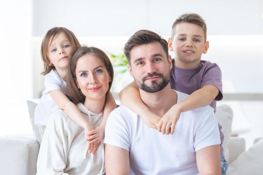 Family portrait of young parents with their two children at home, white modern desgin of living room