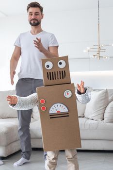 Happy family father and son playing dancing like robots at home, children wearing handmade moving box costume of cardboard