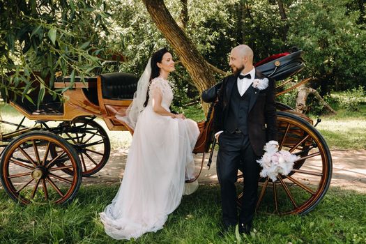 A couple of the bride and groom are standing near the carriage in nature in retro style.