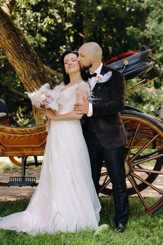 A couple of the bride and groom are standing near the carriage in nature in retro style.