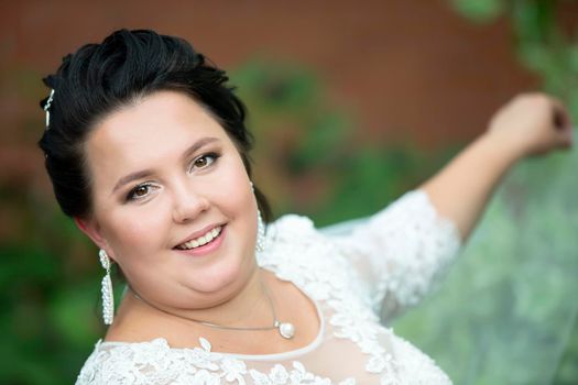 Close-up portrait of a fat bride.Portrait of a plump bride with a waving veil against a background of summer greenery.