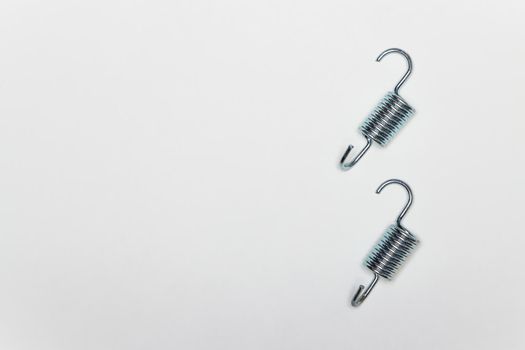 Two short metal springs for repairing the brakes of the machine. Set of spare parts for car brake repair. Details on white background, copy space available. UHD 4K.