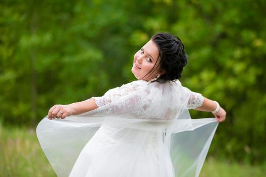 Portrait of a plump bride with a waving veil against a background of summer greenery.