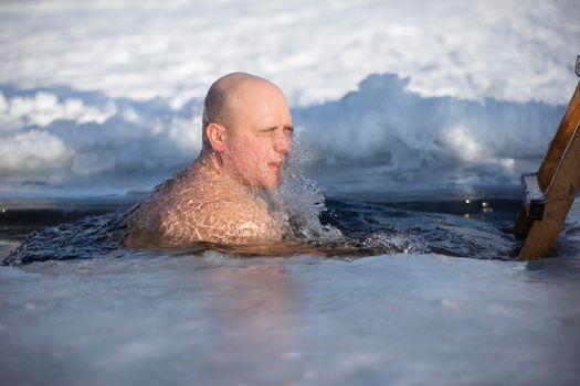 A man plunges into an ice-hole during the winter festival of the baptism of Jesus. A man swims in the ice-hole in winter. Walrus people.
