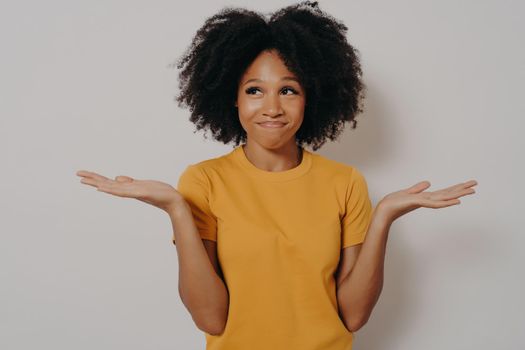 Young african american woman standing in casual clothes with clueless and funny confused expression with arms and hands raised, isolated over white studio background. Positive body language concept