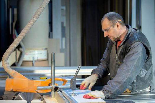 A furniture manufacturing worker at a cutting machine makes furniture parts. Furniture manufacturing.