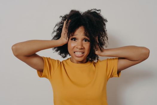 African American distressed young woman losing control over emotions, closing her ears with hands tightly, showing I can not stand it anymore gesture. Isolated over white background with copy space