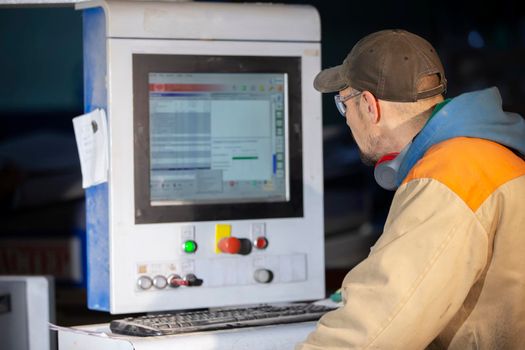 A furniture production worker behind a programmed machine makes furniture parts. Furniture manufacturing.