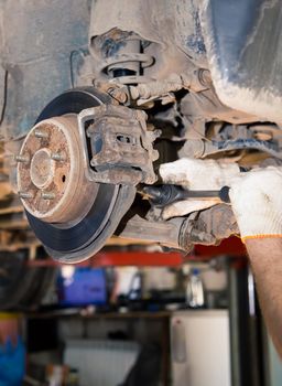 The gloved hands of a man unscrew the rusty caliper on the hub with a wrench. In the garage, a man changes parts on a vehicle. Small business concept, car repair and maintenance service. UHD 4K.