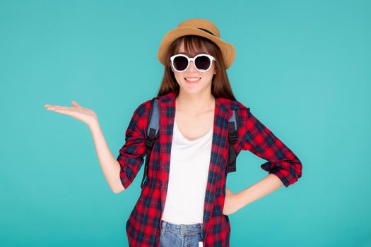 Beautiful portrait young asian woman wear sunglasses and hat smile and enjoy in summer gesture presenting something isolated on blue background, tourist girl in vacation travel concept.