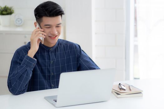 Young asian man talking phone and work from home with laptop computer, freelance using notebook to internet online and speak on smartphone, domestic life, business and communication concept.