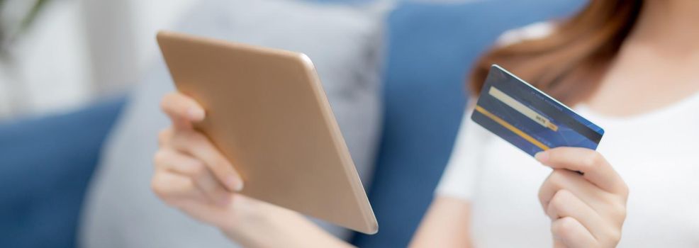 Young asian woman smiling holding credit card shopping online with tablet computer buying and payment, girl using debit card purchase or transaction of finance, lifestyle and e-commerce concept.