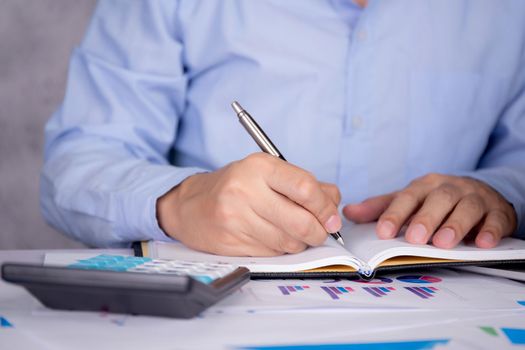 Hands of businessman calculate tax with calculator while laptop computer on desk, man planning finance and investment with graph and chart, statistic and examining account, business concept.