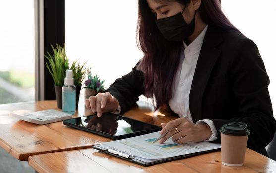 Side view of asian businesswoman wearing face mask while working on a computer for financial calculations in the office. hygiene and safety concept