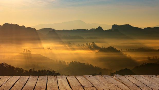 Wooden terrace with mountain landscape and sunrise.
