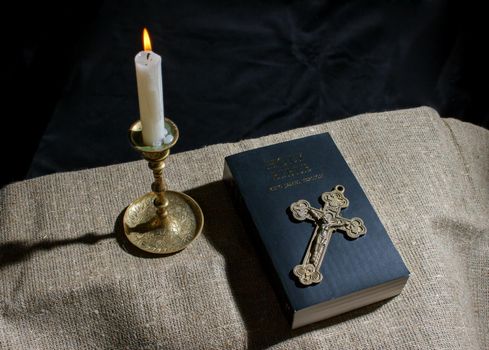 bronze cross, burning candle and bible on the table indoor closeup