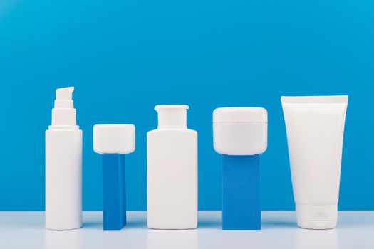 Set of white unbranded cosmetic bottles for daily skincare on geometric props for product presentation against bright blue background. Concept of hygiene, man's skin care or anti acne treatment