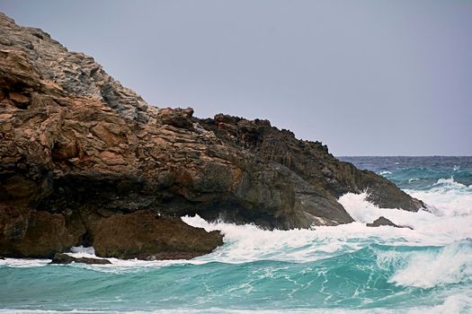 Rocks on the shore hit by the waves. Balearic Islands, Mediterranean Sea, blue sky, splashes of water.