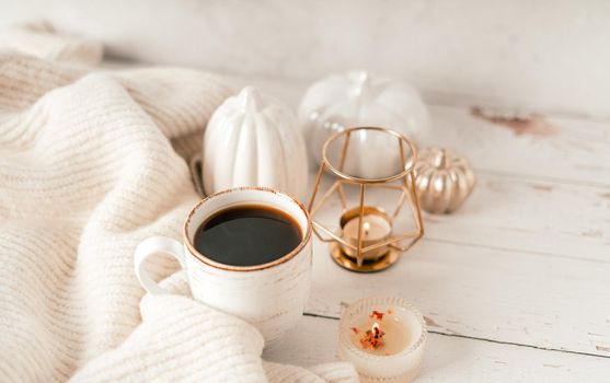 Details of Still life, cup of tea or coffee, pumpkins, candle, brunch with leaves on white table background, home decor in a cozy house. Autumn weekend concept. Fallen leaves and home decoration