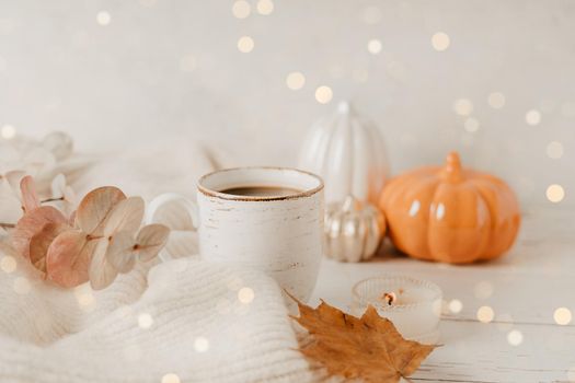 Details of Still life, cup of tea or coffee, pumpkins, candle, brunch with leaves on white table background, home decor in a cozy house. Autumn weekend concept. Fallen leaves and home decoration