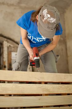 Ukraine, Goshcha, voluntary event, - August, 2021 - skilled young female worker is using power screwdriver drilling during construction wooden bench, gender equality, feminism