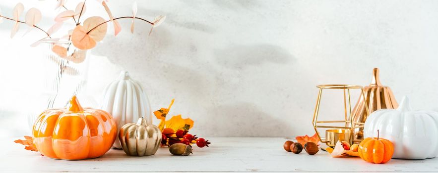 Details of Still life, pumpkins, candle, brunch with leaves on white table background, home decor in a cozy house. Autumn weekend concept. Fallen leaves and home decoration