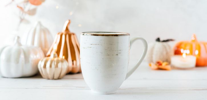 Details of Still life, cup of tea or coffee, pumpkins, candle, brunch with leaves on white table background, home decor in a cozy house. Autumn weekend concept. Fallen leaves and home decoration