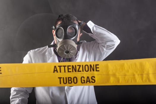 A medical engineer wearing antigas mask experienced in the gas leaks crisis directing the emergency during the chaos. On the yellow tape the written notice "attention gas tube"