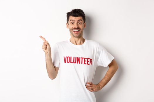 Happy smiling volunteer pointing finger left at copy space, showing announcement, white background.