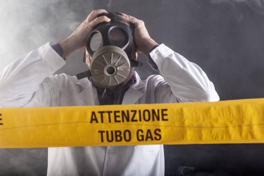 A medical engineer wearing antigas mask experienced in the gas leaks crisis directing the emergency during the chaos. On the yellow tape the written notice "attention gas tube"