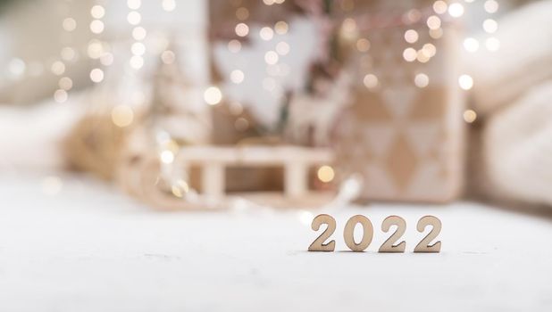 Christmas background or greeting card with 2022 wooden text and copy space. Glowing snow bokeh. Winter holidays on white background.