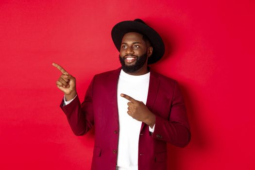 Winter holidays and shopping concept. Happy Black man pointing left and smiling, showing new year promo offer on red background.