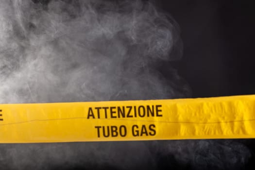 Yellow emergency sign of attention gas pipe on smoke-filled background. On the yellow tape the written notice "attention gas tube"