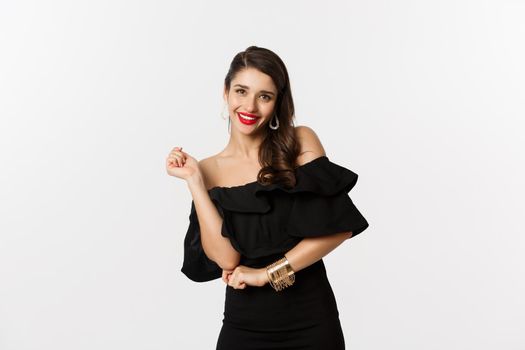 Fashion and beauty. Woman celebrating and dancing in black dress, having fun and smiling, standing over white background.