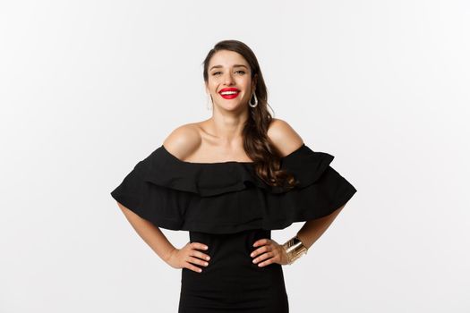 Beauty and fashion concept. Elegant young woman wearing party dress and red lipstick, laughing at camera, standing cheerful against white background.