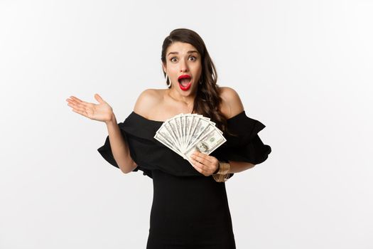 Beauty and shopping concept. Excited lucky woman winning money, looking amazed and holding dollars, standing over white background.