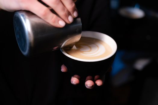 latte art by barista. pouring milk in coffee. dark coffee house.