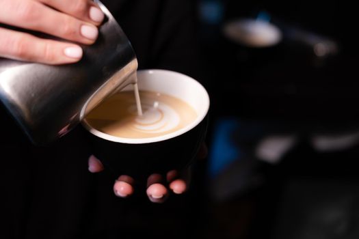 latte art by barista. pouring milk in coffee. dark coffee house.